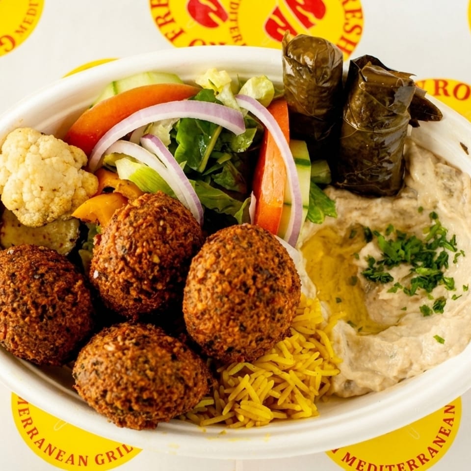 Mediterranean gyro bowl with falafel, yellow rice, hummus, stuffed grape leaves, roasted vegetables, and fresh salad.