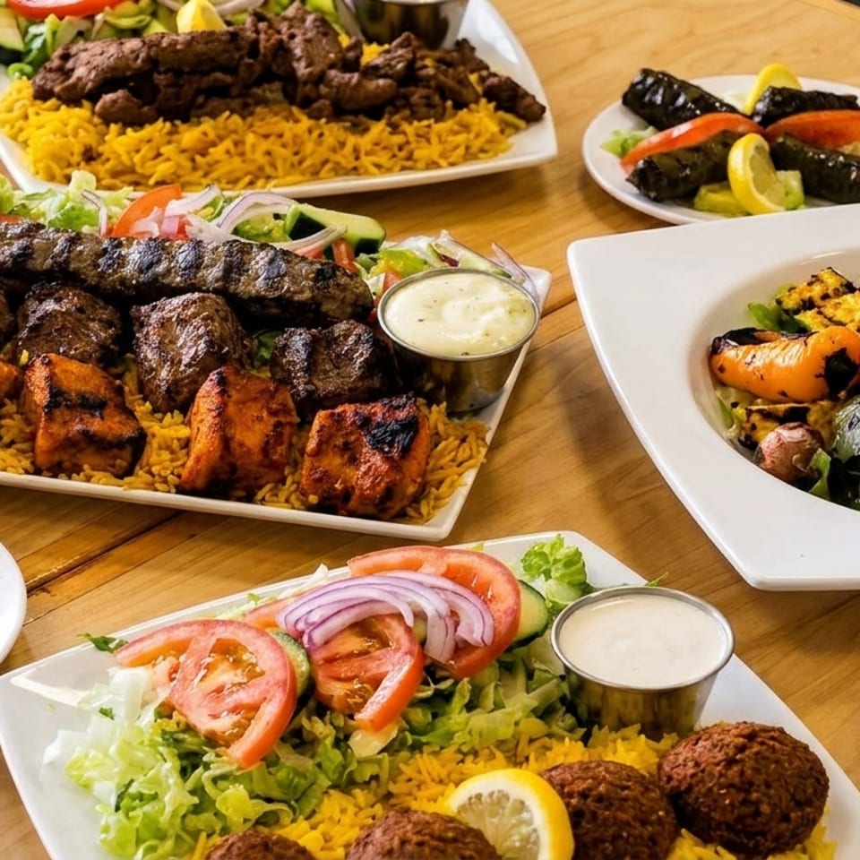 Assortment of Middle Eastern dishes featuring grilled meats, yellow rice, hummus, salad, roasted vegetables, and dipping sauces on a wooden table.