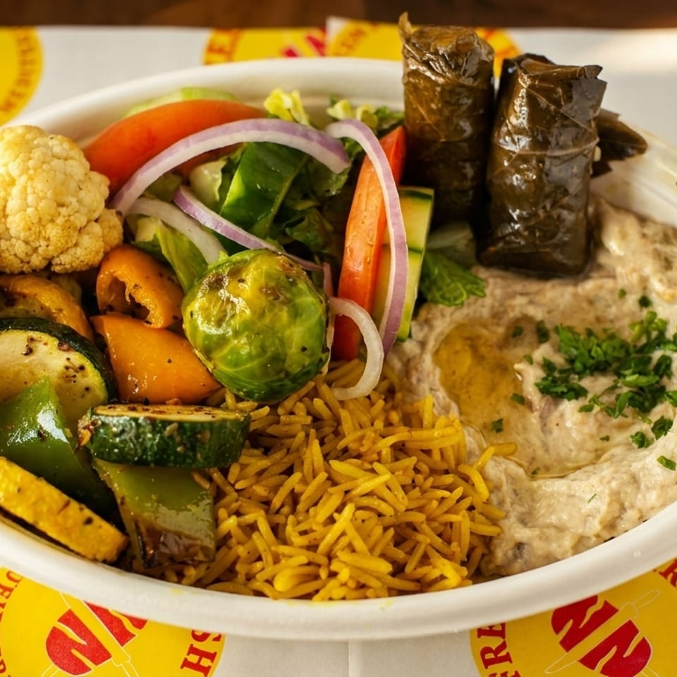 Mediterranean platter with rice, hummus, stuffed grape leaves, fresh salad, and roasted vegetables in a bowl.